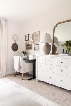 a bedroom with white furniture and pictures hanging on the wall, along with a large mirror