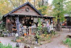 a small wooden building with lots of plants and decorations on the outside wall, in front of trees