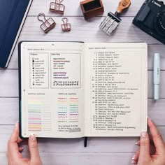 a person holding an open book on top of a wooden table next to other items