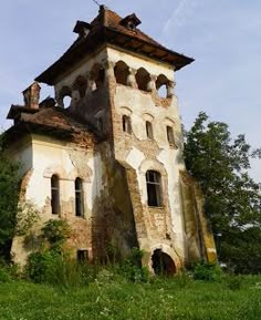 an old building sitting on top of a lush green field next to trees and bushes