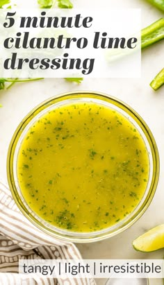 a bowl filled with green liquid next to asparagus and lemons on a table