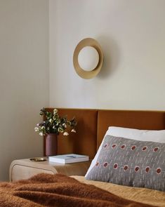 a bed with a brown headboard and white pillows on top of it next to a small table with flowers