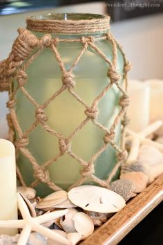 a green glass jar sitting on top of a wooden tray filled with seashells