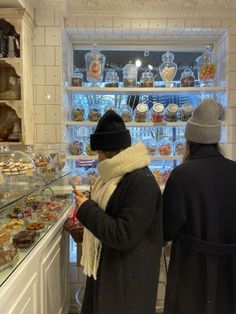 two people standing in front of a display case filled with pastries and desserts