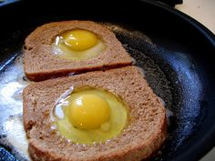 two slices of bread with eggs on them in a frying pan, ready to be cooked