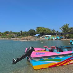 a colorful boat sitting on top of a body of water next to a shore line