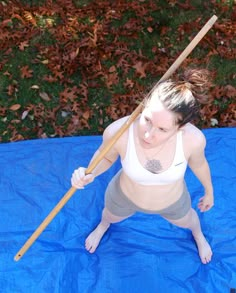 a woman holding a baseball bat on top of a blue tarp covered ground with leaves in the background