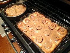 two pans filled with cinnamon rolls sitting on top of an open stovetop oven