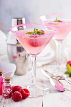 two martinis with raspberries and mint garnish on the side, ready to be served