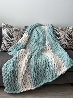 a blue and white knitted blanket sitting on top of a couch next to pillows