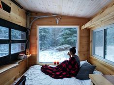 a woman sitting on top of a bed next to a window in a room filled with wooden walls