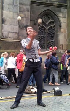 a man juggling balls on the street in front of a building with people standing around