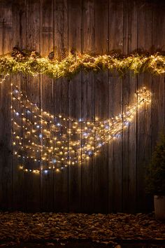 a wooden fence covered in christmas lights next to a potted plant