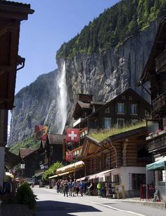 people are walking down the street in front of some buildings with a waterfall behind them