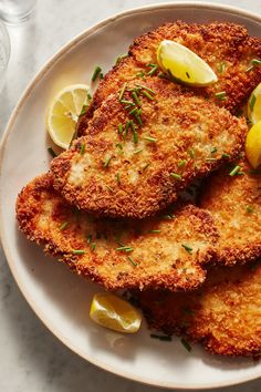 some fried food on a plate with lemon wedges