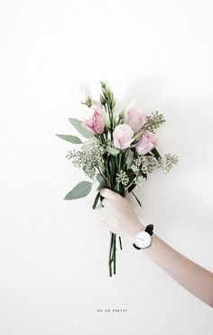 a person holding a bouquet of flowers in front of a white wall with a quote on it