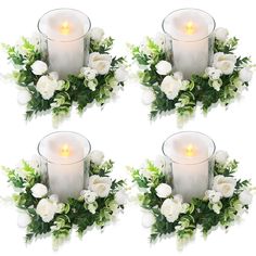 four white roses and greenery are arranged in the shape of a wreath with a lit candle