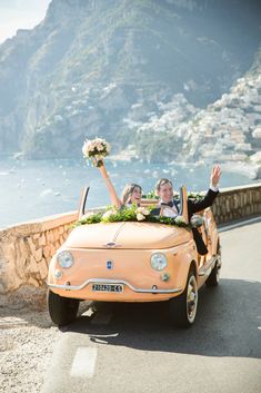 a bride and groom ride in an orange convertible car with flowers on the roof as they wave to the crowd