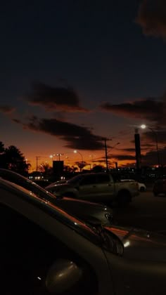 cars parked in a parking lot at night with the sun going down and clouds lit up