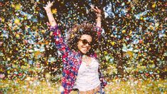 a woman standing in the grass with her hands up and confetti all around her