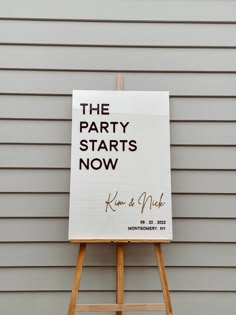 the party starts now sign is on an easel in front of a gray wall