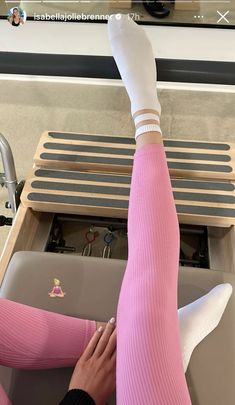 a woman in pink pants and white socks is holding her leg up with both hands