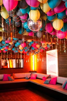 a room filled with lots of balloons hanging from the ceiling and couches covered in pillows