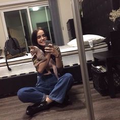 a woman sitting on the floor holding a cat and taking a selfie in front of a mirror