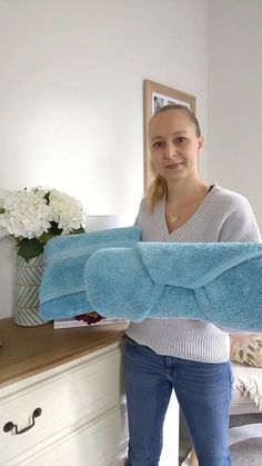 a woman standing in front of a bed holding a blue towel