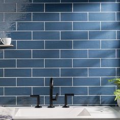 a kitchen sink with two black faucets and a blue brick wall behind it