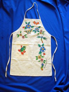 an apron with embroidered flowers and birds on it, sitting on a blue cloth background