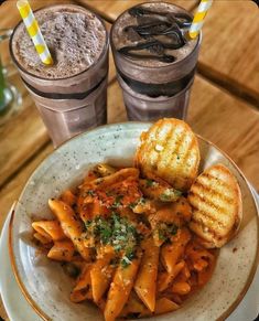 a plate with pasta, bread and two drinks on a table next to each other