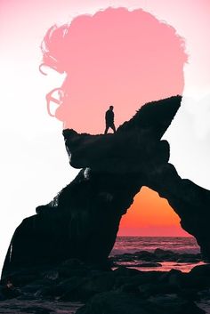 a person standing on top of a large rock formation near the ocean at sunset or sunrise