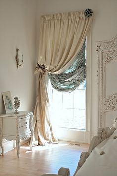 a bedroom with a bed, dresser and window covered in draping on the curtains