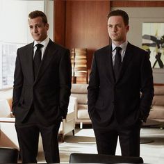 two men in suits standing next to each other near a table with chairs and couches