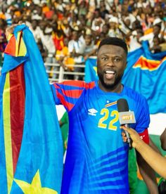 a man holding a microphone in front of an audience at a sporting event with flags