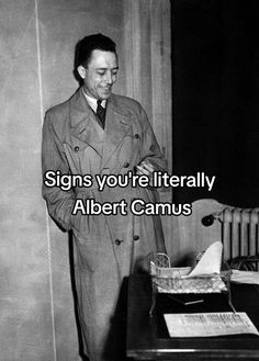 a man standing next to a desk in front of a sign that says signs you're literally albert camus