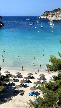 many people are on the beach with umbrellas and boats in the water behind them