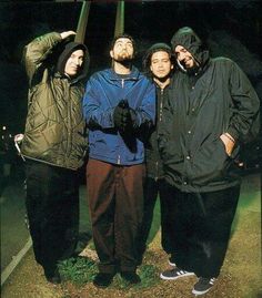 three men standing next to each other in front of a street sign at night with their eyes closed