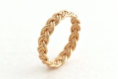 a gold ring with an intricate braid design on the inside and outside, sitting on a white surface