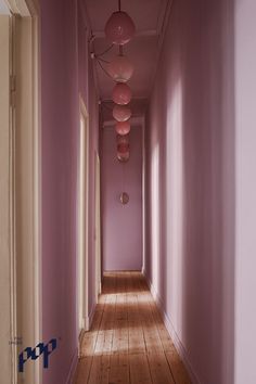 a long hallway with pink walls and wooden flooring is lit by three hanging lamps