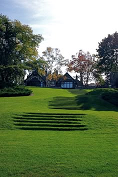 a large grassy field with steps leading up to the house and trees in the background