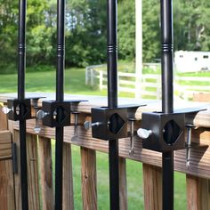 four black metal brackets are on the side of a wooden fence with grass and trees in the background