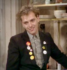 a man in a suit with buttons on his lapel smiles at the camera while sitting down