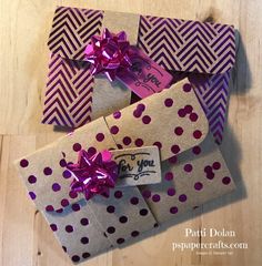 three wrapped gift boxes with purple polka dots and pink ribbon tied around the top, sitting on a wooden surface