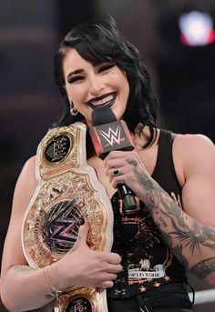 a woman holding a microphone and wearing a wrestling belt