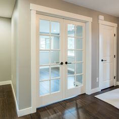 an empty room with white doors and wood flooring on the side, leading to another room