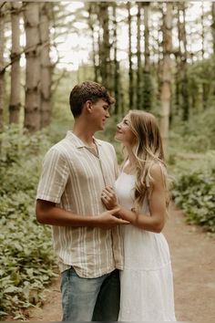 a young man and woman standing together in the woods looking into each other's eyes