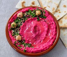 a bowl filled with hummus and garnish next to pita bread