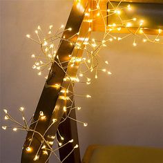 a ladder is decorated with lights in the shape of leaves and branches, along with a yellow chair